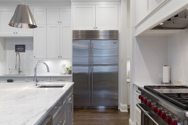 silver refrigerator in a white kitchen with stove and sink