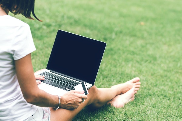 woman sitting in grass with a laptop and holding a credit card