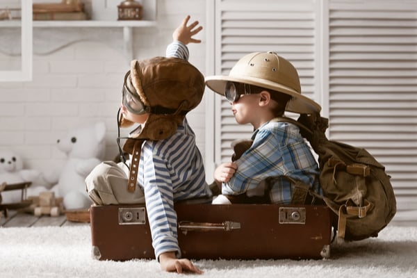 2 kids dressed up as explorers pretending to fly in a suitcase
